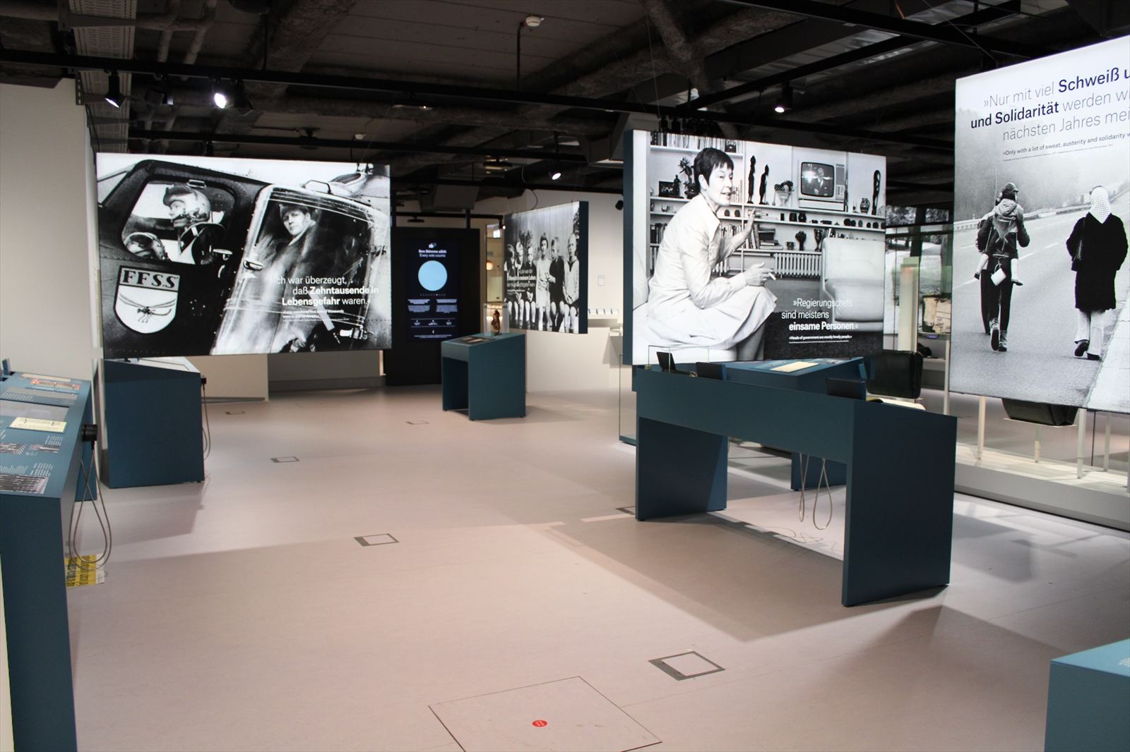 Ausstellungsraum mit großformatigen Leuchtbildern, Medientischen und Kopfhörern